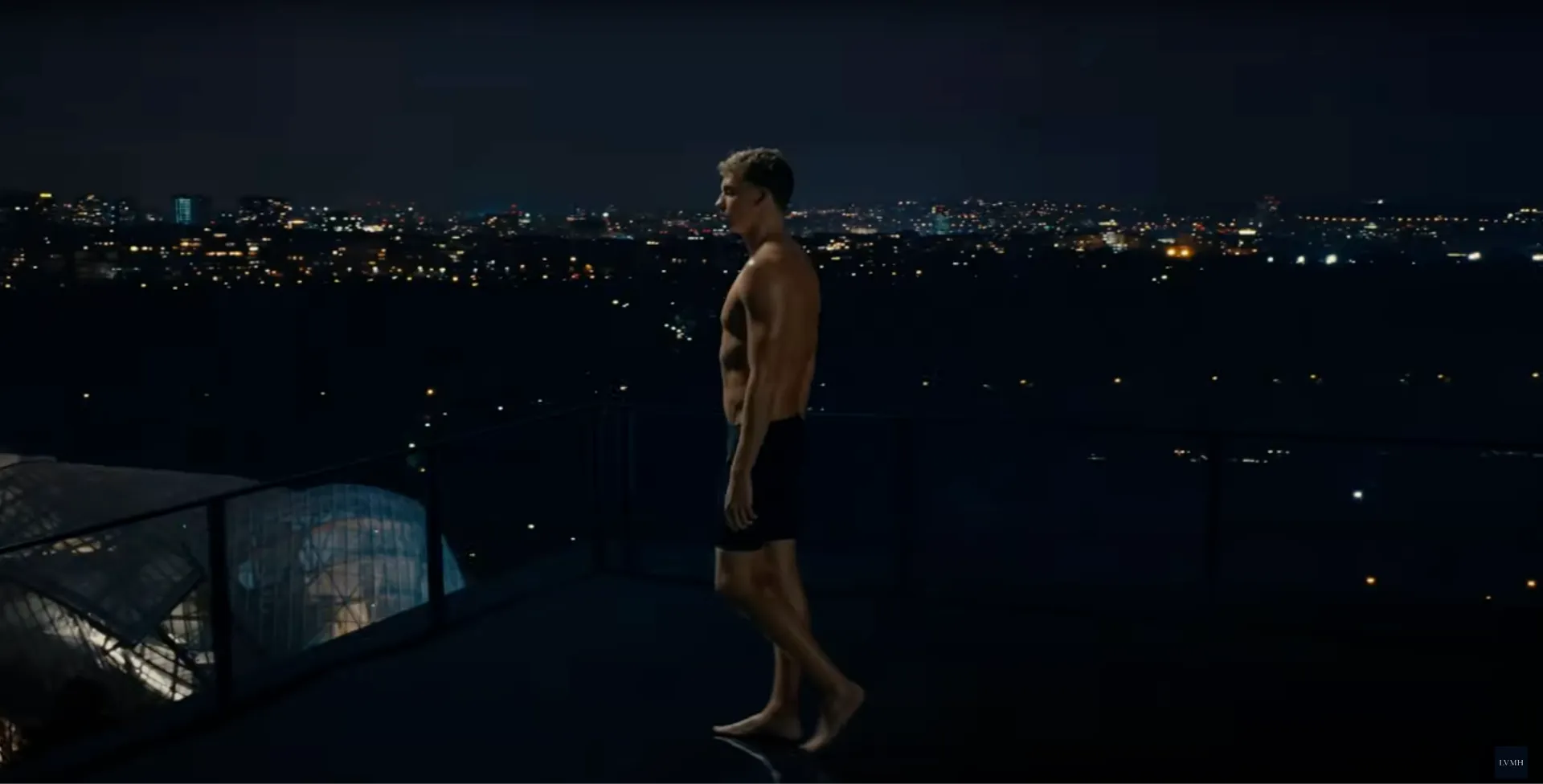 Image du film LVMH "À nous deux, Paris !" : un nageur debout sur un toit de Paris, la ville illuminée derrière lui